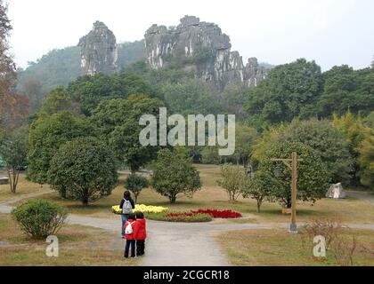 Persone che camminano nei giardini del Seven Star Park a Guilin nella provincia di Guangxi, Cina. Alle spalle si trova la famosa formazione carsica del Camel Hill. Foto Stock