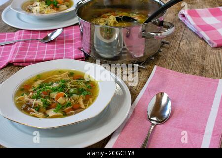 tavolo da pranzo con zuppa di pollo con piatto, cucchiaio, pentola Foto Stock