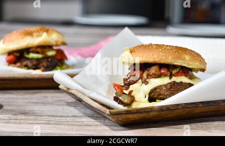 delizioso cheeseburger gourmet con cipolle rosse caramellate smaltate, formaggio svizzero, sottaceti e pomodori filettati Foto Stock