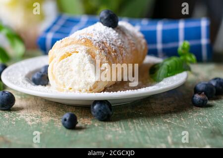 un rotolo di pasta sfoglia con ripieno di crema su un po' piatto bianco servito su un tavolo di legno verde Foto Stock