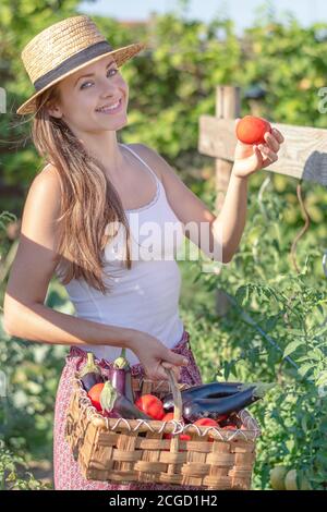 Estate in giardino. Giovane bella donna che tiene il cesto pieno di verdure appena raccolte nel suo giardino. Concetto di produzione biologica locale. Foto Stock