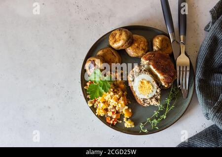 Uova di scotch fatte in casa su un piatto di ceramica servite con pilaf di bulgur, funghi alla griglia ed erbe aromatiche. Cotoletta di carne con uovo bollito. Tradizionale Foto Stock