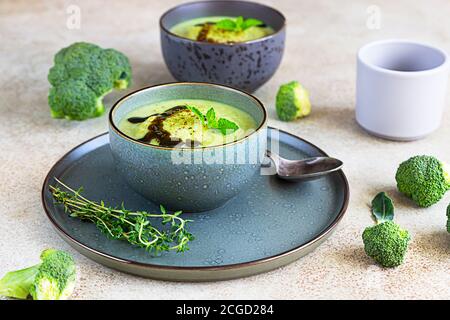 Broccoli o zuppa verde di spinaci con olio aromatizzato speziato nel recipiente. Cibo vegano sano. Sfondo di pietra. Messa a fuoco selettiva. Foto Stock