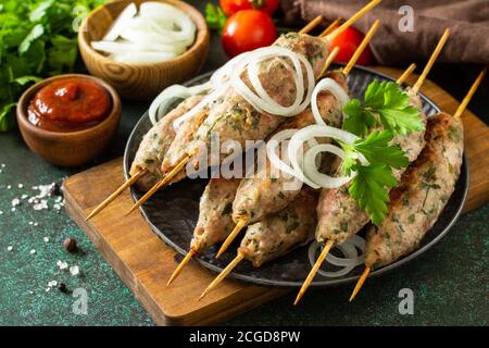 Kebab turco. Kebab Kofta fatti in casa su uno spiedino con verdure e salsa su uno sfondo di pietra o ardesia. Foto Stock