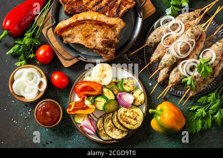 Kebab Kofta fatti in casa, bistecca alla griglia e verdure alla griglia su uno spiedino con verdure e salsa su uno sfondo di pietra o ardesia. Vista dall'alto, disposizione piatta b Foto Stock