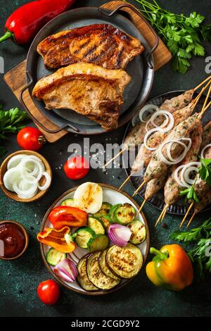 Kebab Kofta fatti in casa, bistecca alla griglia e verdure alla griglia su uno spiedino con verdure e salsa su uno sfondo di pietra o ardesia. Vista dall'alto, disposizione piatta b Foto Stock