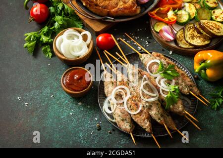 Kebab Kofta fatti in casa, bistecca alla griglia e verdure alla griglia su uno spiedino con verdure e salsa su uno sfondo di pietra o ardesia. Spazio di copia. Foto Stock