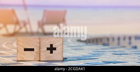 Segno più e meno su cubetti di legno sulla spiaggia rilassata. Concetto di business online Foto Stock