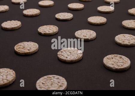 Distribuzione del modello di cracker di riso. Cracker rotondi di riso, sparsi su uno sfondo nero. Design frontale o prospettico. Fotografia low-key. Foto Stock