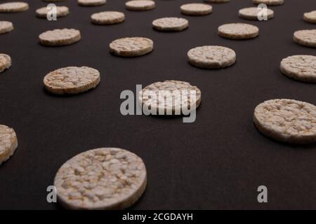 Distribuzione del modello di cracker di riso. Cracker rotondi di riso, sparsi su uno sfondo nero. Design frontale o prospettico. Fotografia low-key. Foto Stock