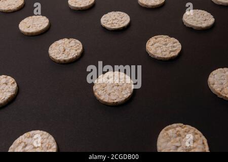 Distribuzione del modello di cracker di riso. Cracker rotondi di riso, sparsi su uno sfondo nero. Design frontale o prospettico. Fotografia low-key. Foto Stock