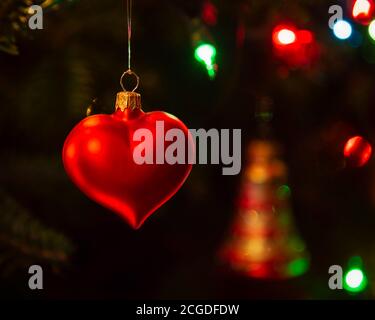 Ornamento natalizio a forma di cuore in vetro appeso in un albero di Natale illuminato in abete balsamo. Foto Stock