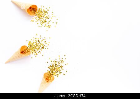 Coni di cialde gialli con nappina di confetti dorati isolati su sfondo bianco. Piatto, vista dall'alto, festivo minimo. Concetto di festa e celebrazione. Foto Stock