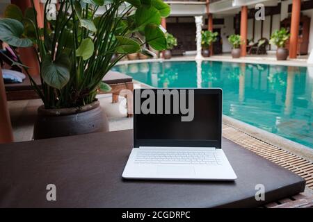 Computer portatile bianco sullo sfondo della piscina. Area di lavoro concettuale. Freelance, viaggi e vacanze. Foto Stock