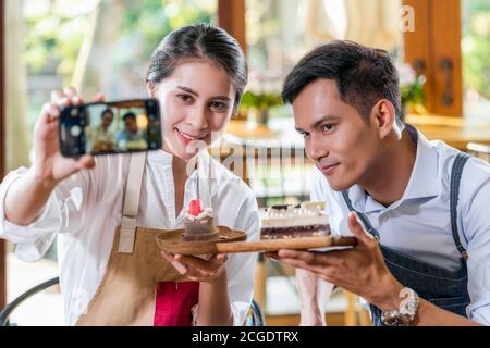 Coppia Asian due partner di piccola impresa proprietario prendendo selfie e presentando la panetteria in caffetteria quando reccord vlog, torta e dessert, entrepren Foto Stock