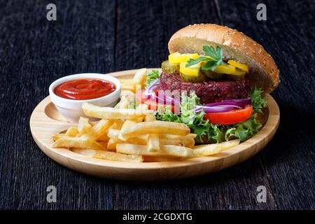 Hamburger di barbabietola vegana con sottaceti lattuga fresca, pomodori, cipolle rosse, frittura francese, ketchup su un piatto di bambù su un tavolo di legno scuro, vista dall'alto, primo piano Foto Stock