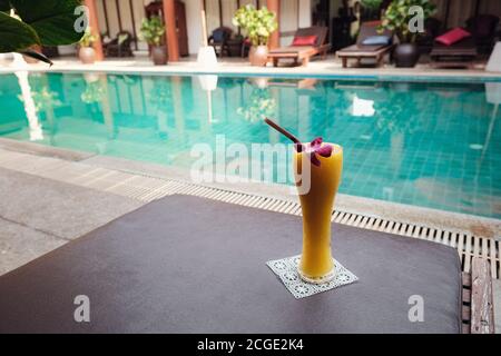 frullato tropicale fresco o succo di mango in un bicchiere alto sullo sfondo della piscina Foto Stock