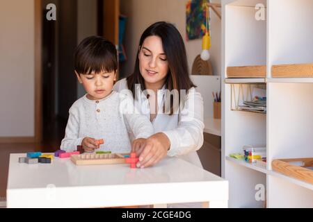 Lillte Kid giocare con un puzzle di legno di tetris e la madre o l'aiuto dell'insegnante. Homeshooling. Comunità di apprendimento. Scuola Montessori Foto Stock