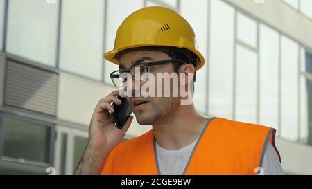 Ispettore ingegnere nervoso in hardhat che parla al telefono. Foto Stock