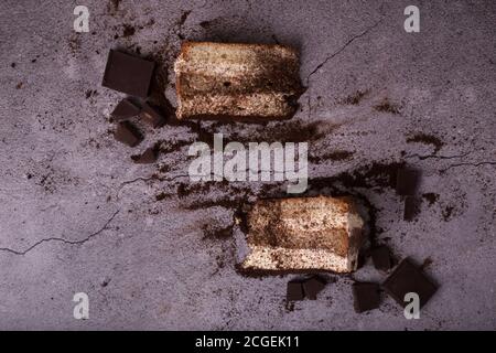 Tradizionale tiramisù dessert italiano. Alcuni pezzi sul tavolo sono sparsi e cioccolato. Vista dall'alto Foto Stock