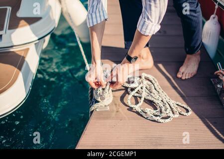 Mano dell'uomo con corda della barca. Lo yachtsman ormora la sua barca a motore al molo. Chiudi le mani e prua della barca. Foto Stock