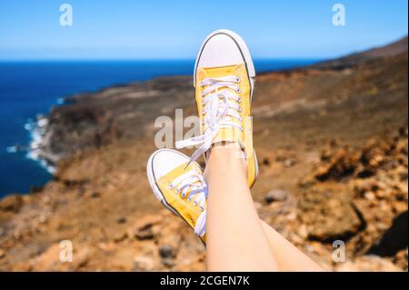 Vista ravvicinata, dei piedi della donna che indossano sneakers . Il viaggiatore si siede su Rock indossando sneaker gialle. Vacanze estive. Foto Stock