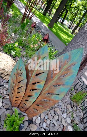 Decorazione di foglie di ferro su un letto di fiori nel parco. Le foglie di ferro sono un elemento dell'arredamento estivo del parco cittadino. Foto Stock