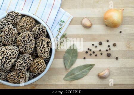 Funghi porcini primaverili commestibili appena raccolti in una ciotola in ceramica su un tagliere con spezie. Primo piano, vista dall'alto. Foto Stock