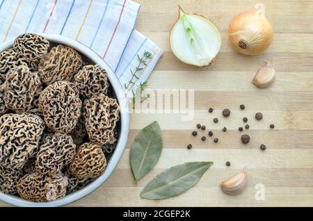 Funghi porcini primaverili commestibili appena raccolti in una ciotola in ceramica su un tagliere con spezie. Primo piano, vista dall'alto. Foto Stock