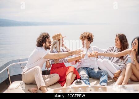 Giovani turisti europei di ragazzi e ragazze che celebra su yacht avvio felice della loro vacanza - Gruppo di amici di tostatura e bevande aventi parte su una ISC Foto Stock