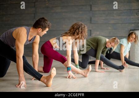 Gruppo di principianti di yoga maschili e femminili che si esercitano contro la parete grigia, facendo yoga o pilates postura. In piedi in posa Guerriero, Virabhadrasana. Full le Foto Stock