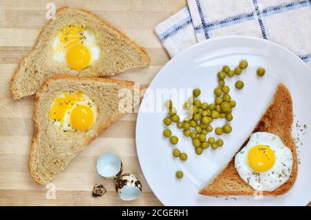 Tostatura con uova di quaglia fritte e piselli verdi su un piatto bianco su un tagliere di legno, vista dall'alto. Cibo sano. Foto Stock