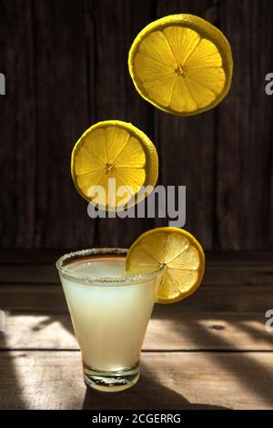 tre fette di limone mature e succose rotonde volano e cadono in un cocktail in un bicchiere con zucchero sul bordo su un tavolo di legno, foto orizzontale per il menu del bar Foto Stock