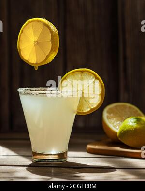 le fette di limone, tonde, mature e succose, volano e cadono in un cocktail in un bicchiere con zucchero sul bordo su un tavolo di legno, foto orizzontale per il menu del bar Foto Stock