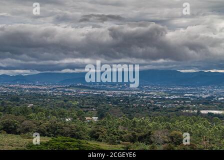 Provincia di Alajuela, Costa Rica - 28 novembre 2008: Skyline di San Jose City nella sua valle sotto il folto paesaggio torbido, visto dalle montagne. Verde Foto Stock