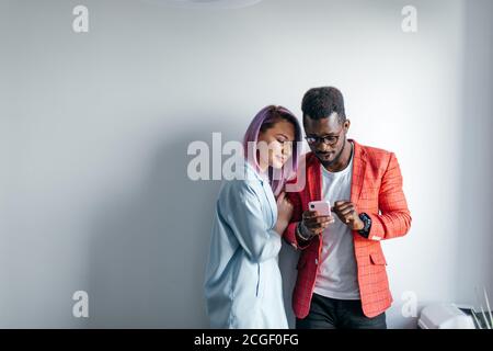 Multirazziale amici la condivisione di foto con ciascun altro, isolato in piedi oltre il muro grigio sfondo, copia dello spazio. Foto Stock