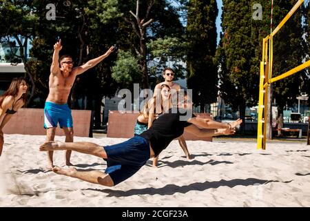 Beach dilettanti giocatori di pallavolo in occhiali da sole e shorts saltando, in piedi in posizione di difesa sul campo di sabbia. Azione sportiva dinamica in prossimità della rete, Foto Stock