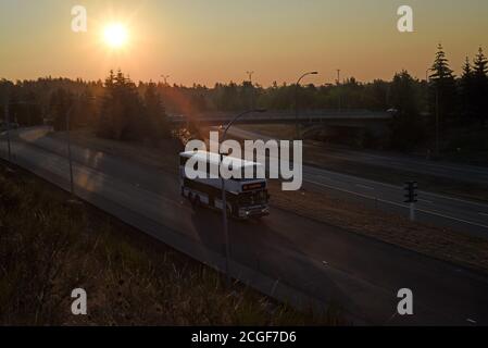 Il sole che sorge al mattino è diffuso dal fumo di fuoco, mentre un autobus a due piani scende lungo una rampa per l'autostrada 1 vicino a Victoria, British Columbia, Canada Foto Stock