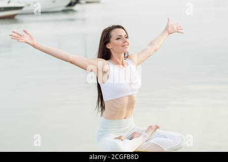 Sporty giovane donna in vestito bianco seduto sulla pietra gialla al mare, godendo il vento fresco del mare e la calma seascape. Yoga, Fitness, Sport all'aperto. Vaca Foto Stock