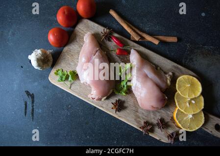Filetti di pollo crudi su un tagliere di legno con ingredienti per cucinare su fondo nero Foto Stock