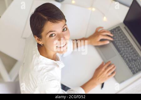 Allegro e sorridente freelance che lavora su un computer portatile nel comfort di casa sua Foto Stock