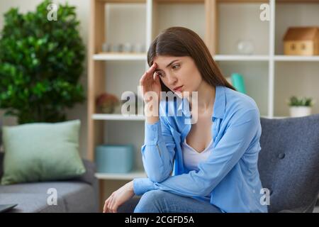 Giovane donna triste che si sente male e che tocca la fronte con la mano Foto Stock