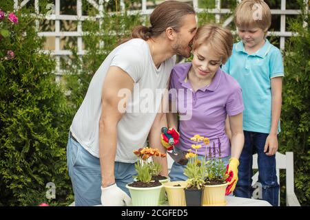 Famiglia felice con un ragazzo di 8 anni visita piantando giardino per acquistare alcuni fiori per il loro giardino, marito amorevole baciare sua moglie mentre insegnano Foto Stock