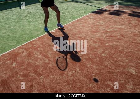 donna irriconoscibile prende una pausa tra le partite di tennis sul campo rosso , l'ombra del giocatore riflessa su un terreno rosso Foto Stock