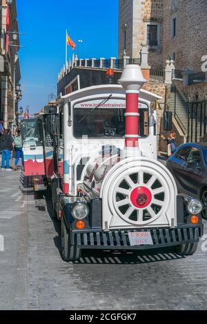 TOLEDO, SPAGNA - 16 febbraio 2020: Passeggiata turistica in una strada del quartiere storico vicino a un piccolo treno turistico rosso in un giorno di primavera Foto Stock