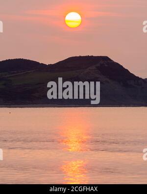 Lyme Regis, Dorset, Regno Unito. 11 Settembre 2020. Regno Unito Meteo. Vista da Lyme Regis in Dorset all'alba come il sole sorge attraverso la sottile nuvola frizzante da dietro Golden Cap sulla Costa Jurassic. Picture Credit: Graham Hunt/Alamy Live News Foto Stock