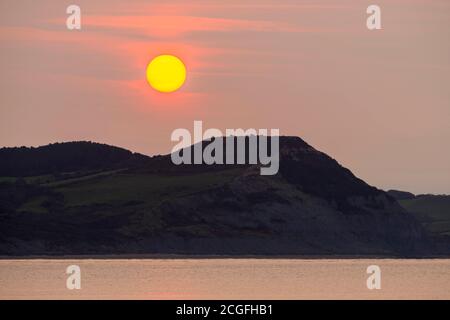 Lyme Regis, Dorset, Regno Unito. 11 Settembre 2020. Regno Unito Meteo. Vista da Lyme Regis in Dorset all'alba come il sole sorge attraverso la sottile nuvola frizzante da dietro Golden Cap sulla Costa Jurassic. Picture Credit: Graham Hunt/Alamy Live News Foto Stock