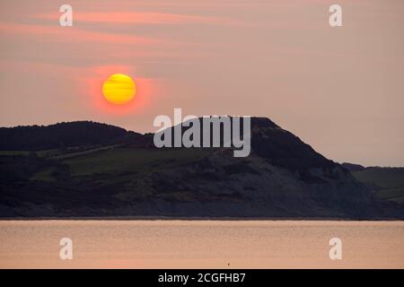 Lyme Regis, Dorset, Regno Unito. 11 Settembre 2020. Regno Unito Meteo. Vista da Lyme Regis in Dorset all'alba come il sole sorge attraverso la sottile nuvola frizzante da dietro Golden Cap sulla Costa Jurassic. Picture Credit: Graham Hunt/Alamy Live News Foto Stock