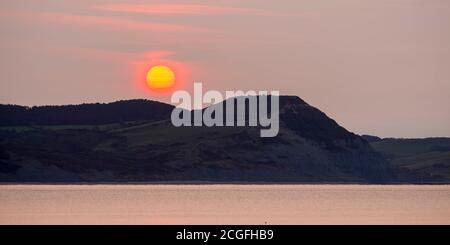 Lyme Regis, Dorset, Regno Unito. 11 Settembre 2020. Regno Unito Meteo. Vista da Lyme Regis in Dorset all'alba come il sole sorge attraverso la sottile nuvola frizzante da dietro Golden Cap sulla Costa Jurassic. Picture Credit: Graham Hunt/Alamy Live News Foto Stock