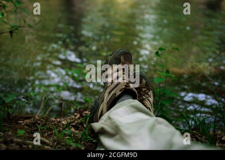 Gambe di un uomo che riposa accanto ad un fiume in foresta. Relax per le gambe. Natura e concetto di riposo. Fermati e rilassati mentre viaggi nella natura Foto Stock